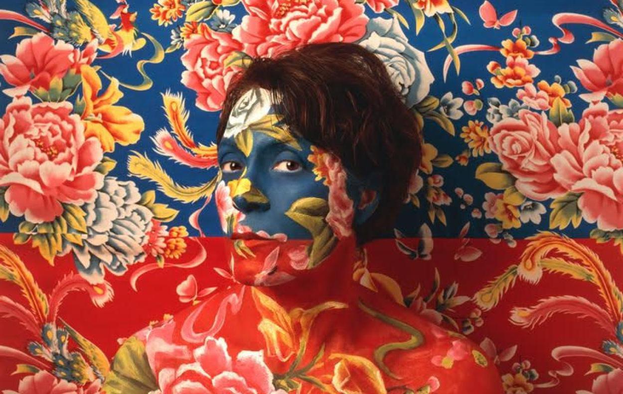 Self Portrait of Artist wearing blue 和 red floral make-up as camouflage with wallpaper behind her